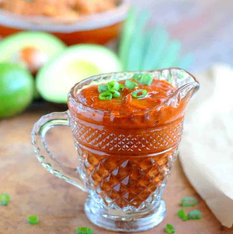 enchilada sauce in a clear serving glass with green onion sliced on top and an avocado in the background.