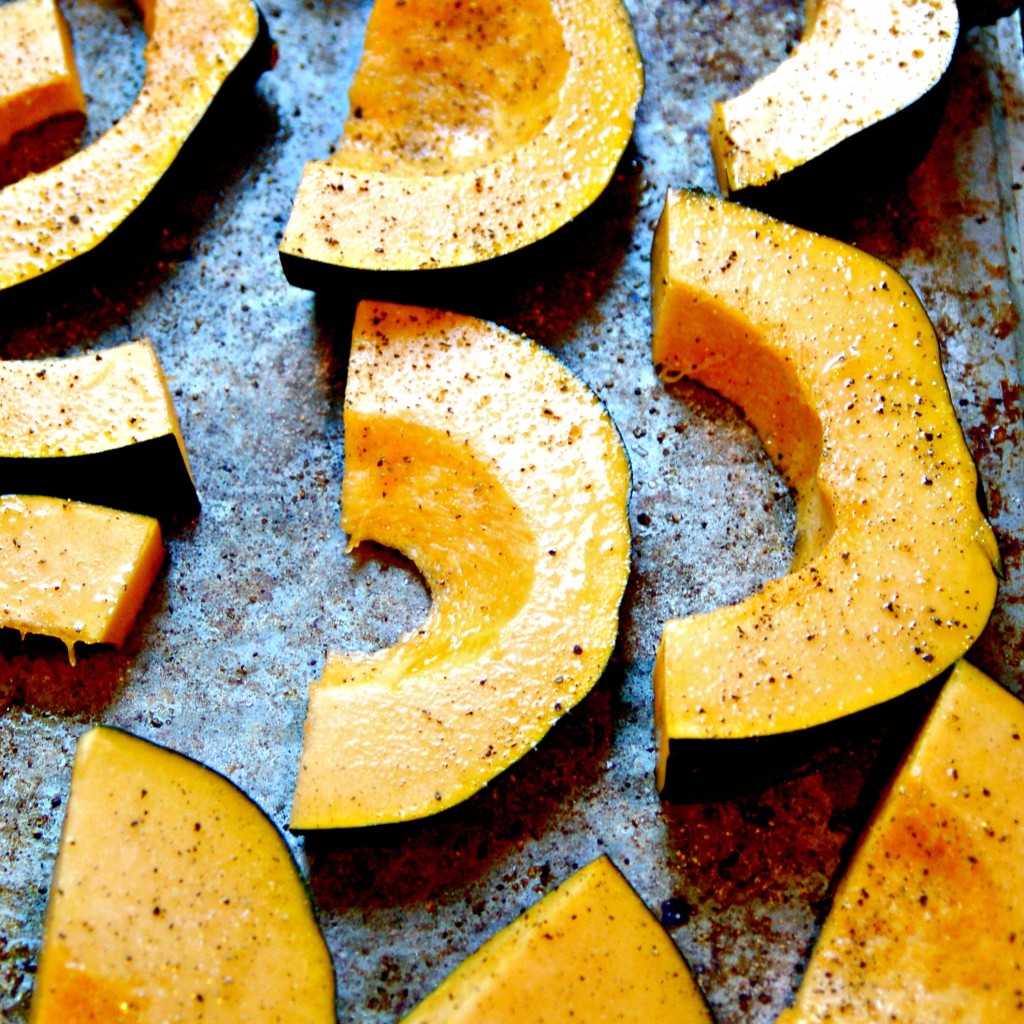 acorn squash shown on a baking pan seasoned with salt and pepper.
