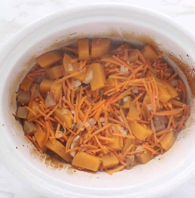 butternut squash soup shown in white slow cooker right after it's done cooking. Showing cooked chunks of butternut squash, carrots, and onions.