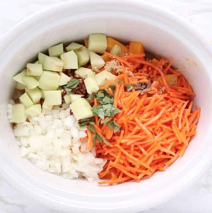 Carrots, apples, onion, and squash is in a white crock pot 