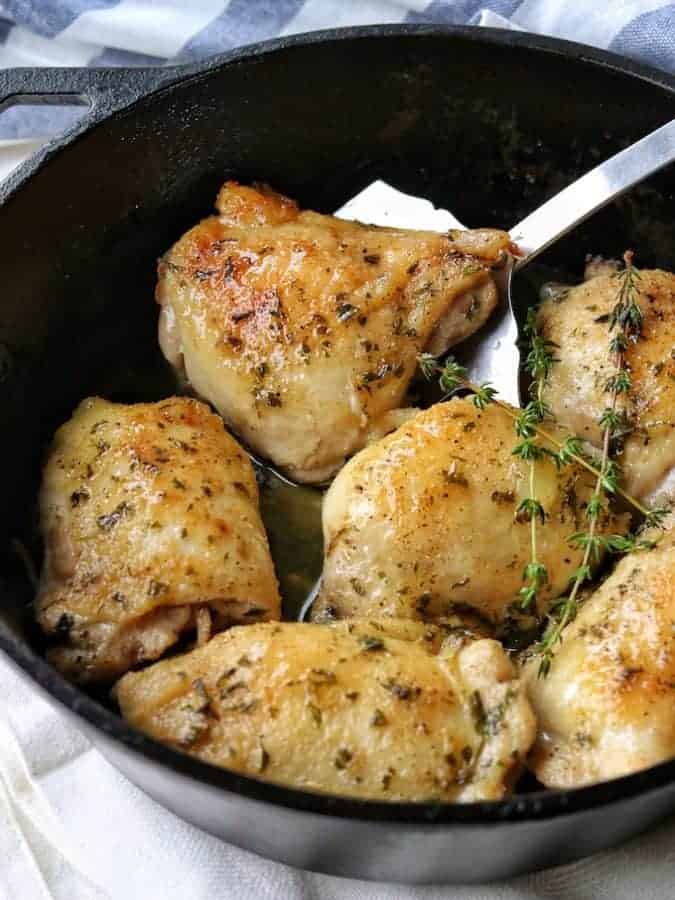 6 baked chicken thighs in a cast iron pan with a metal flipper in the pan lifting a chicken thigh.