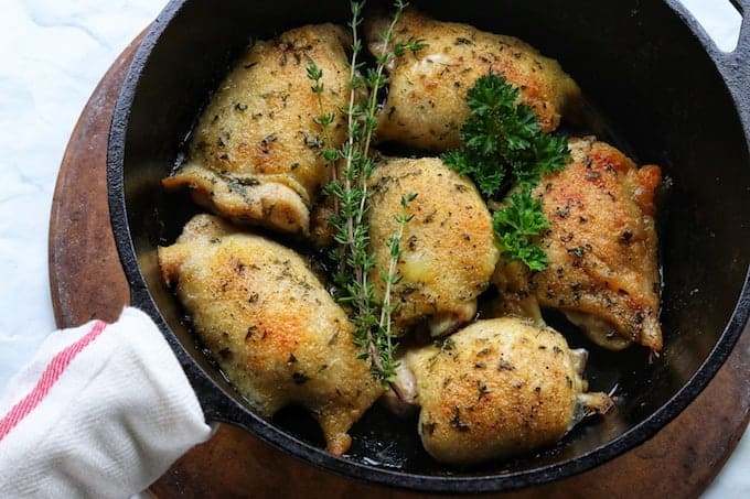 6 baked chicken thighs in a black cast iron pan with fresh herbs on top.
