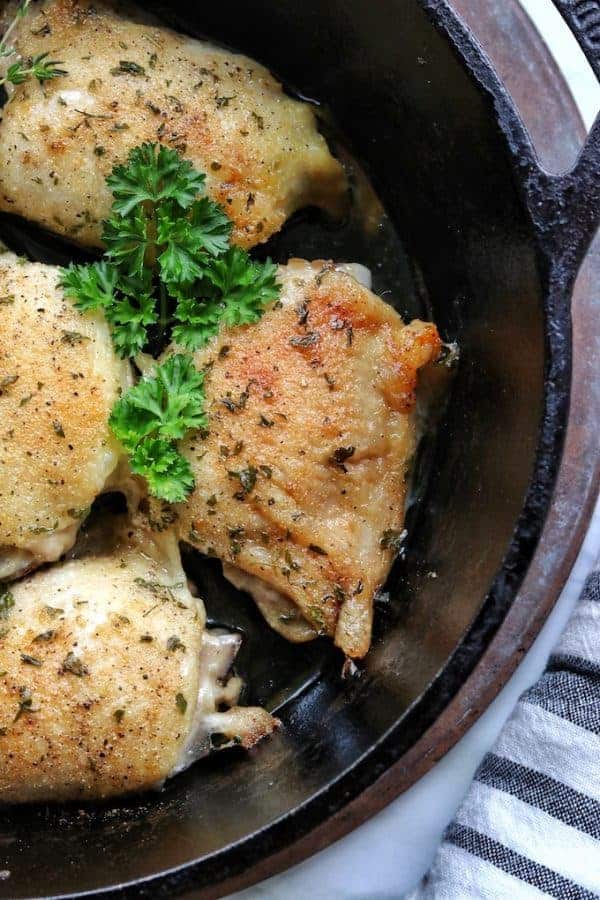 A close up fo 4 baked chicken thighs from the oven in a black cast iron pan with fresh parsley on top.