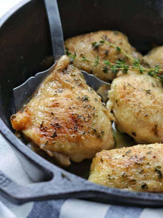 Baked chicken thighs shown up close in a cast iron pan with a close up of a baked chicken thigh with three more next to it in the pan. 