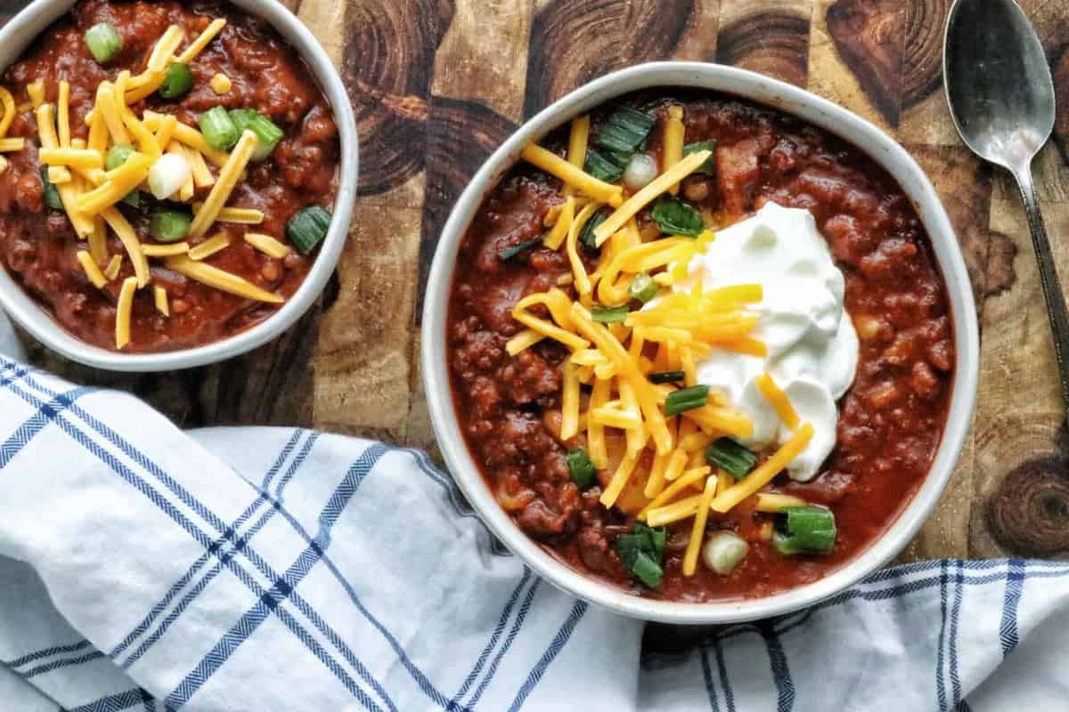top down view of 2 bowls of chili topped with cheese, sour cream, and green onions