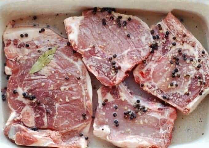 raw pork chops are in a baking dish in a brine.