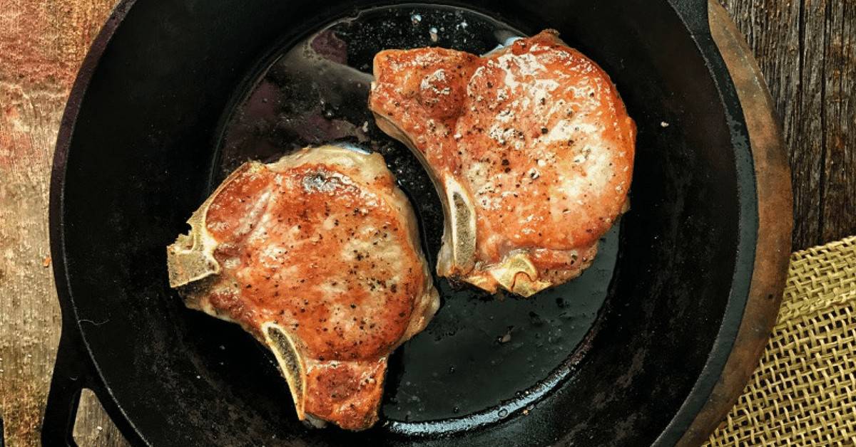 2 seared pork chops are shown in a black cast iron skillet. 