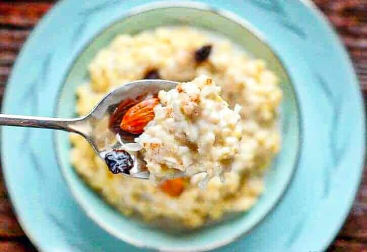 Coconut Millet Breakfast Porridge shown in a blue china bowl with spoon topped with almonds and raisins. 