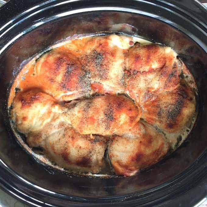 chicken thighs shown seasoned in a black crockpot after being cooked all day.