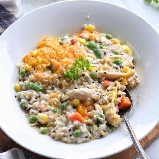 Turkey Rice Casserole in a white bowl including mixed veggies, rice, and cheese in a creamy sauce with a spoon in the bowl. 