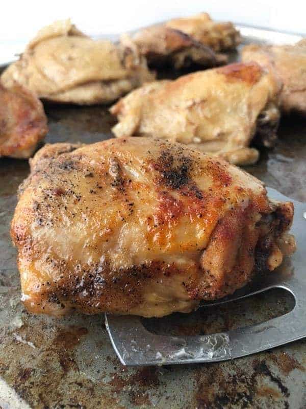 Baked seasoned chicken thighs on a baking pan.