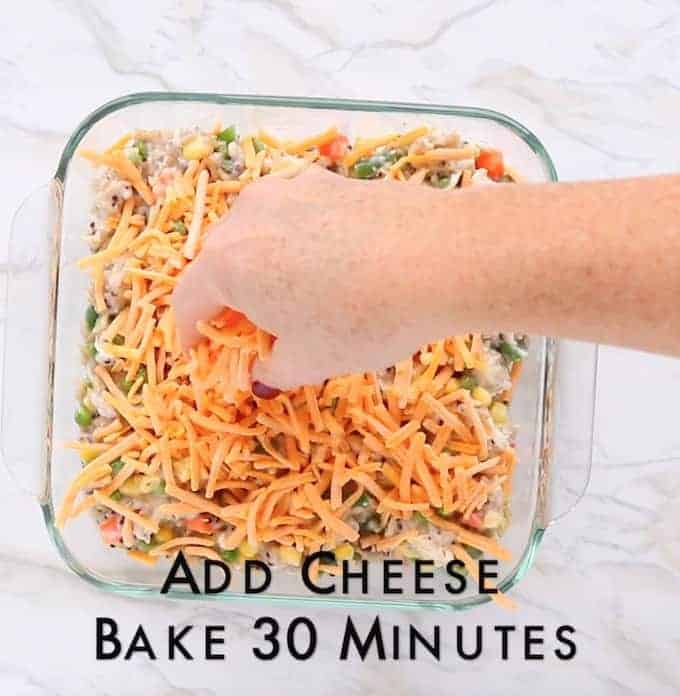 shredded cheese is added to the top of a turkey rice casserole in a clear glass pan.