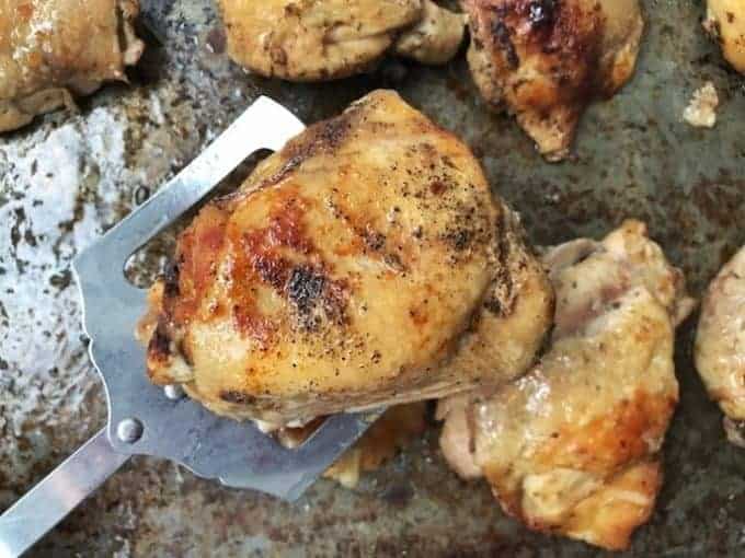 baked bone in skin on chicken thighs on a baking sheet with one chicken thigh resting on a metal spatula. 