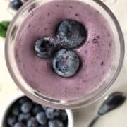 A blueberry smoothie shown up close top down with frozen blueberries on top.