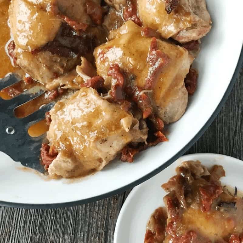 Crock Pot Chicken Thighs shown in a white dish with sun dried tomatoes.