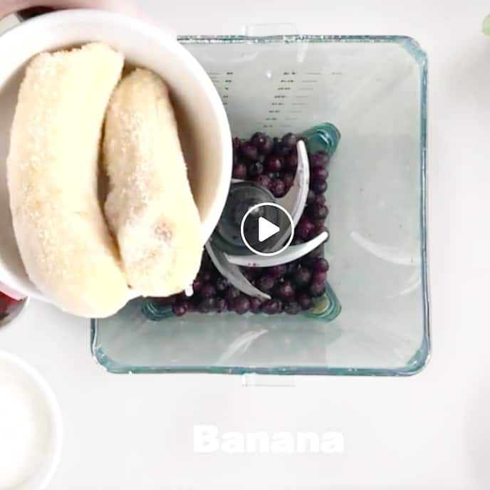 frozen bananas being added to a blender with frozen blueberries in it.