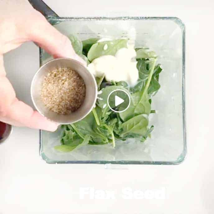 Flax seed being added to a blender with spinach and yogurt.