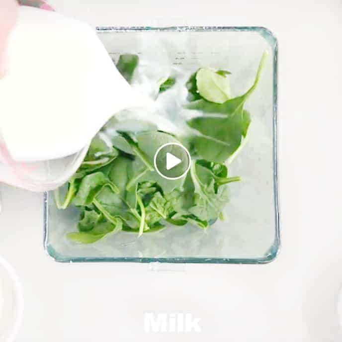 Milk being added to a blender with spinach.