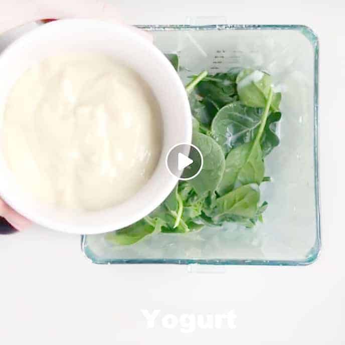 Yogurt being added to a blender with spinach.