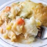 A close up of crustless pot pie showing mashed potatoes with mixed vegetables on a white plate with a fork.