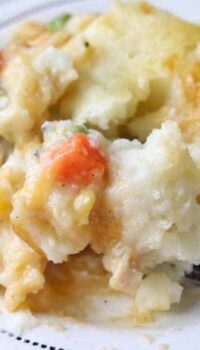 A close up of crustless pot pie showing mashed potatoes with mixed vegetables on a white plate with a fork.