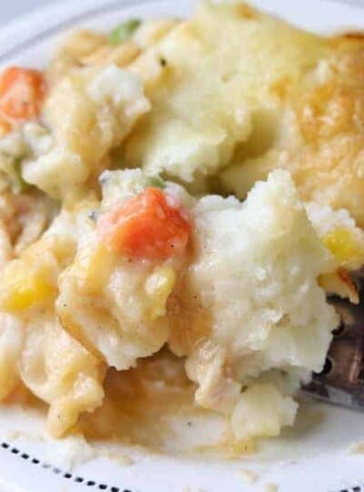 A close up of crustless pot pie showing mashed potatoes with mixed vegetables on a white plate with a fork.