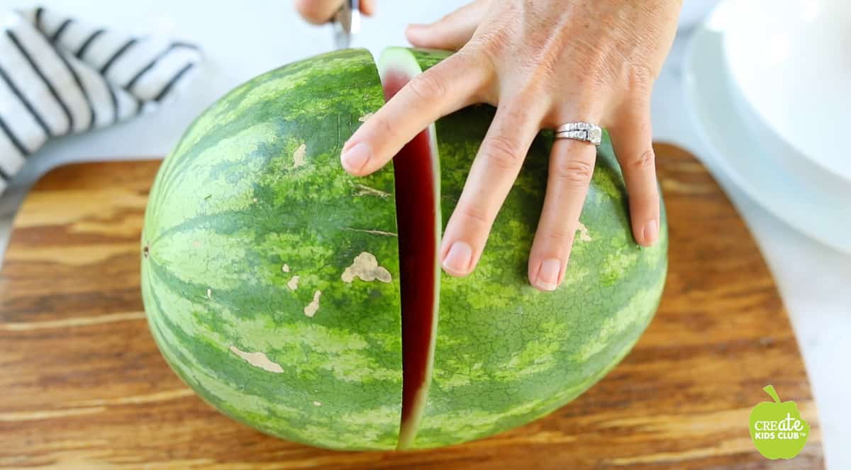 A whole watermelon is being sliced down the middle.