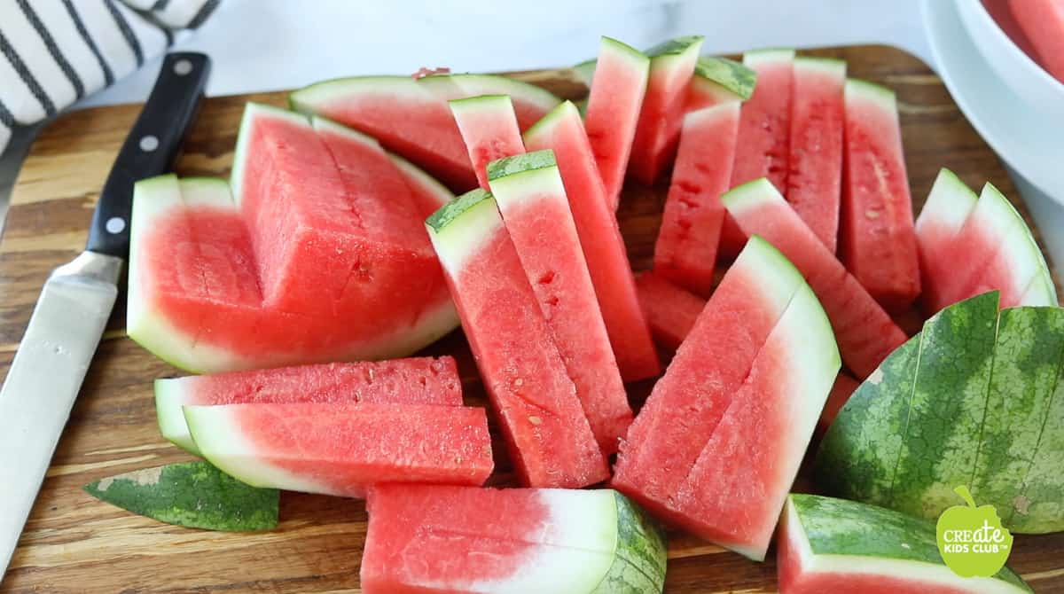 Watermelon sticks are shown after slicing on a wooden cutting board.