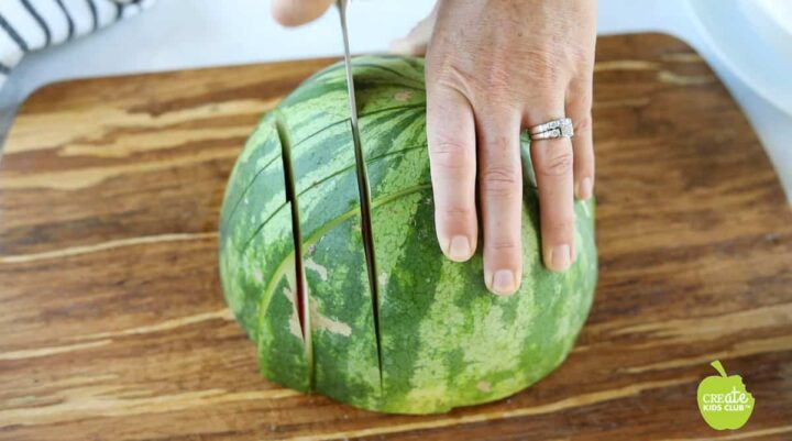 Half of a watermelon is being sliced into tall cube shapes.
