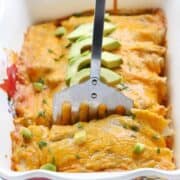 Chicken enchilada casserole shown in a white casserole dish with a spatula taking a piece out.