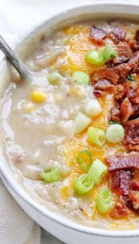 A close up shot of creamy potato soup topped with bacon, melted cheese, and green onion.