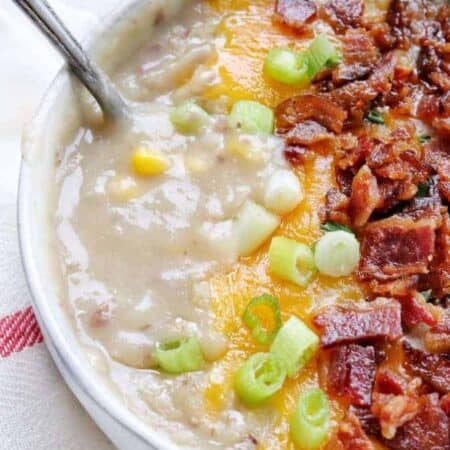 A close up shot of creamy potato soup topped with bacon, melted cheese, and green onion.