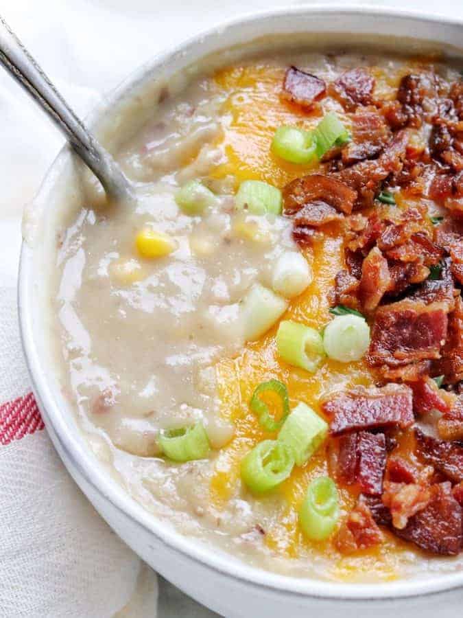 A close up shot of creamy potato soup topped with bacon, melted cheese, and green onion.