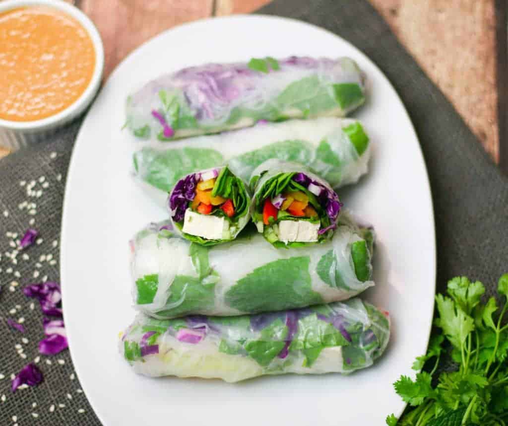 spring rolls shown on a white plate with a sauce next to it.
