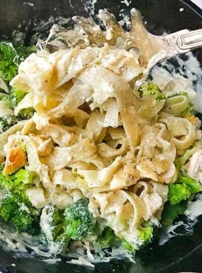 Chicken Alfredo with broccoli and wide noodles shown in a black cast iron skillet.