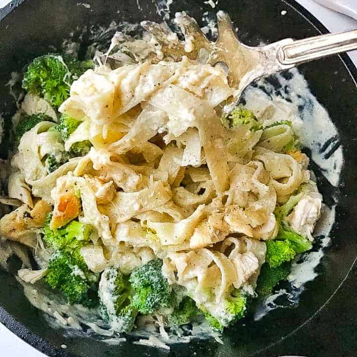 fettuccini alfredo in a sauté pan being stirred with a spoon.