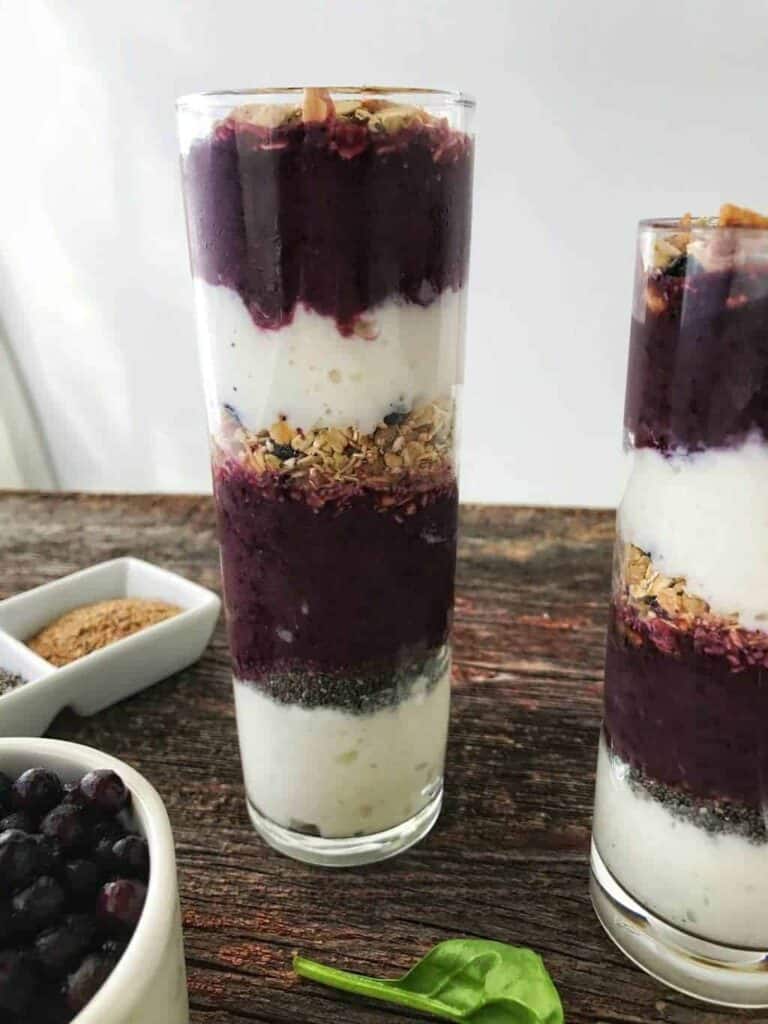 Blueberry & spinach smoothies shown in 2 glasses stacked with cottage cheese, smoothie, cottage cheese on a wooden surface.