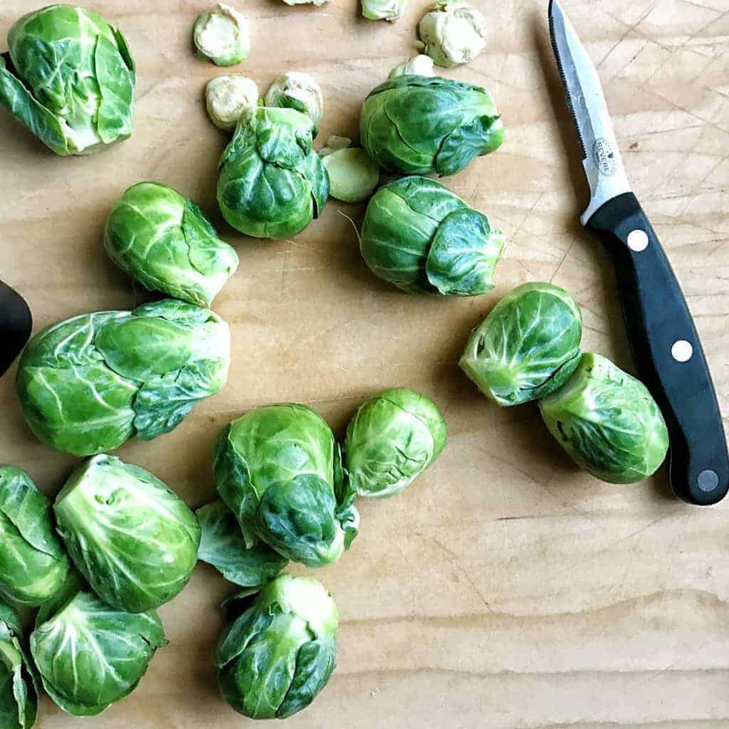 Brussels sprouts shown on a cutting board with a knife.