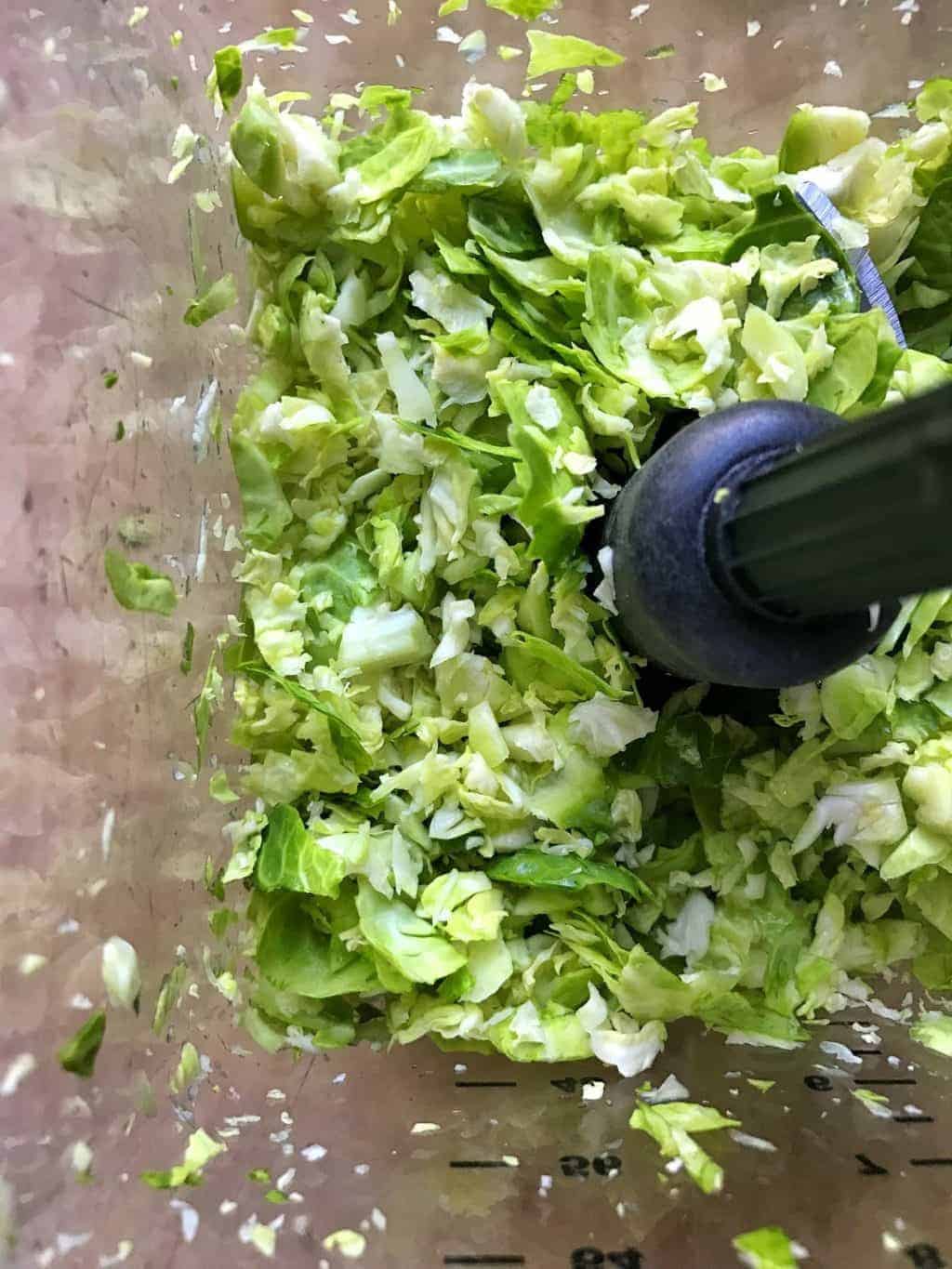 Shredded Brussels sprouts shown in a blender getting shredded.