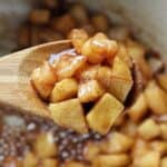 Sautéed diced apples caramelized in a baking pan with wooden spoon.