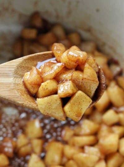 Sautéed diced apples caramelized in a baking pan with wooden spoon.