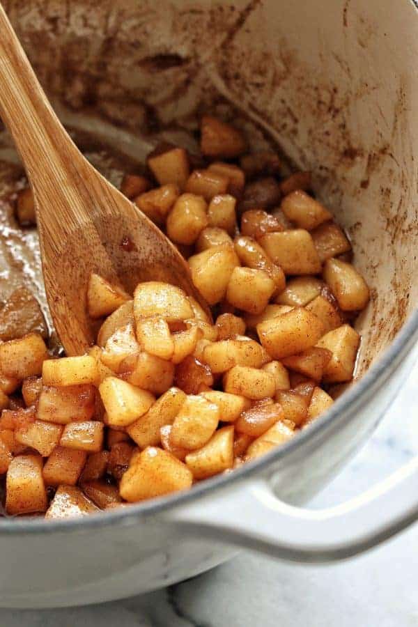 baked apples shown in a white pot with a wooden spoon are simple to make in 10 minutes.