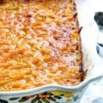 A white casserole dish shown up close with cheesy potatoes hot out of the oven smothered in melted cheese.