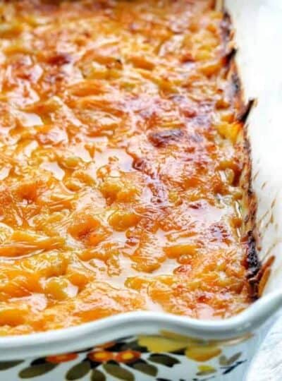 A white casserole dish shown up close with cheesy potatoes hot out of the oven smothered in melted cheese.