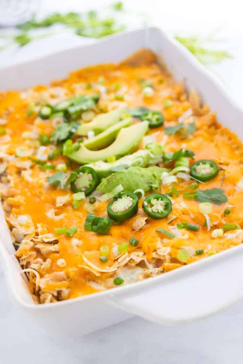 chicken tortilla chip casserole in a pan topped with avocados and jalapenos