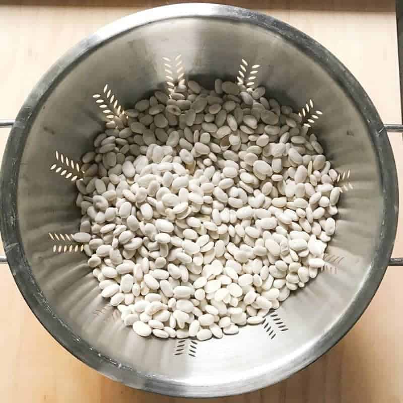 A metal strainer with dry white beans in it. 
