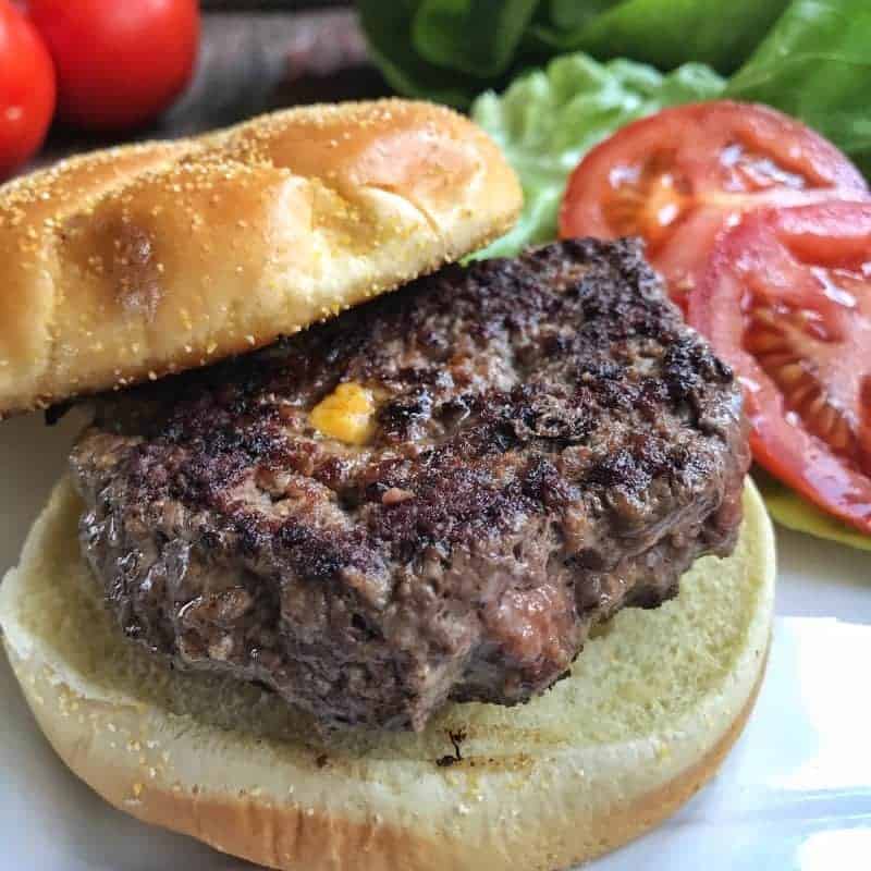 A cheese stuffed burger on a bun with lettuce and tomatoes next to it.
