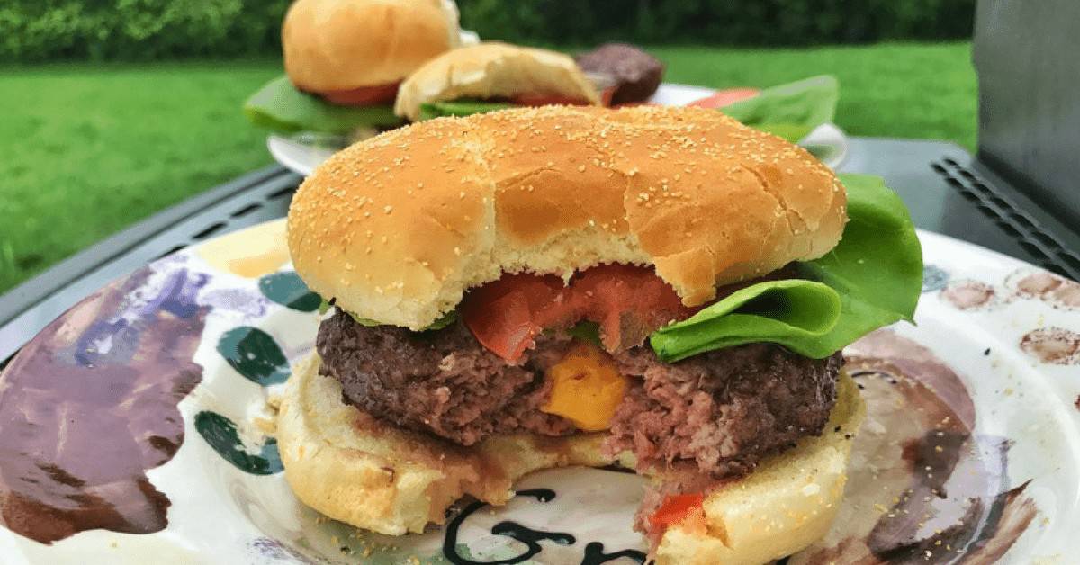 A close up of a bite out of a cheese curd burger.