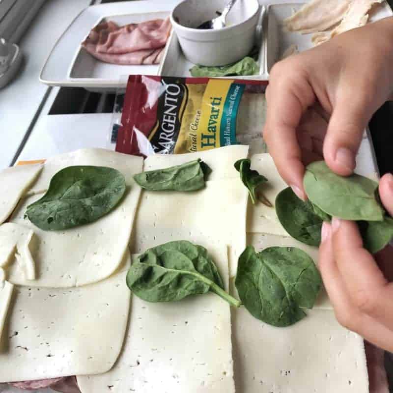 A person putting spinach on a sandwich