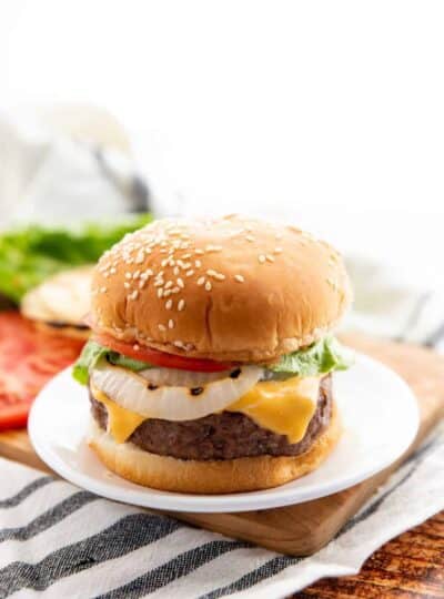 cheese stuffed burgers on a bun with onion, cheese, tomato, and lettuce on a white plate